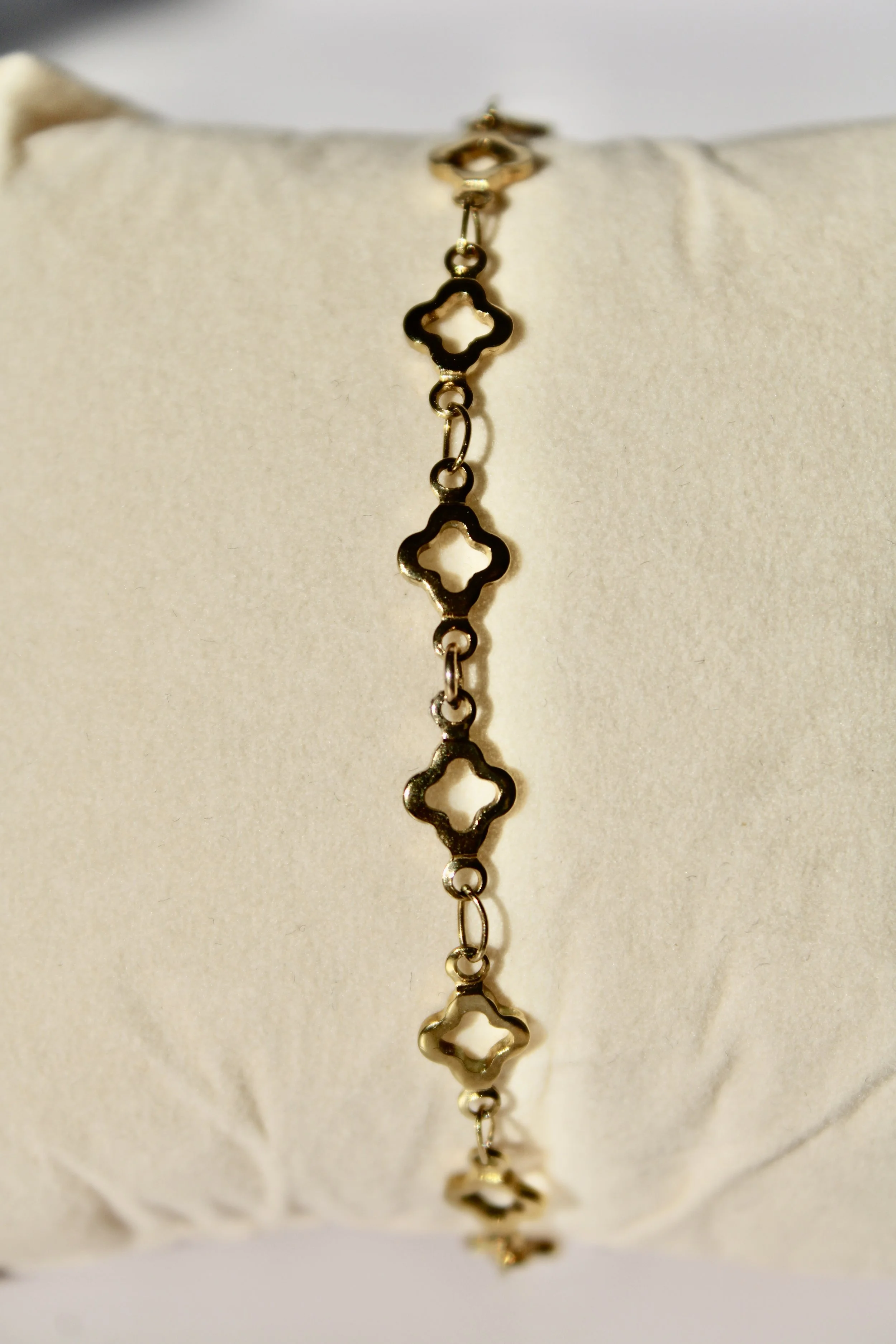 Close-up of a delicate gold bracelet with a series of open, four-leaf clover shaped links, displayed on white fabric.