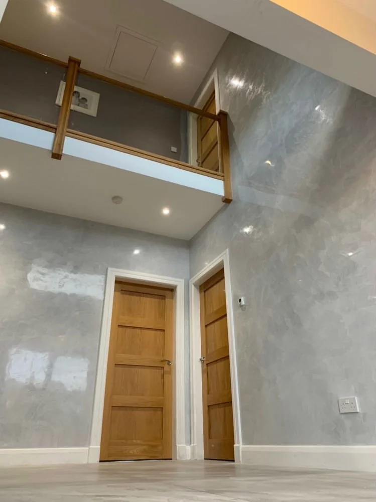 Interior view of a modern home with two wooden doors, a glass-paneled railing on the upper level, and gray marbled walls.
