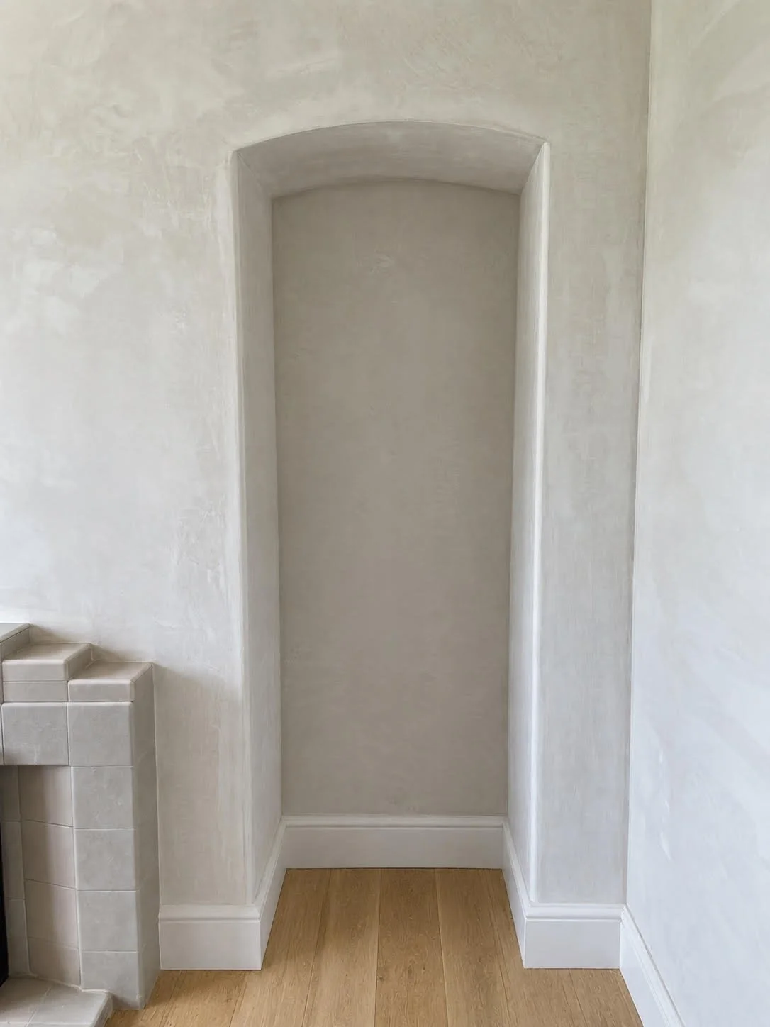 Empty recessed wall niche with rounded top in a light-colored room, with wood flooring and partial view of tiled counter.