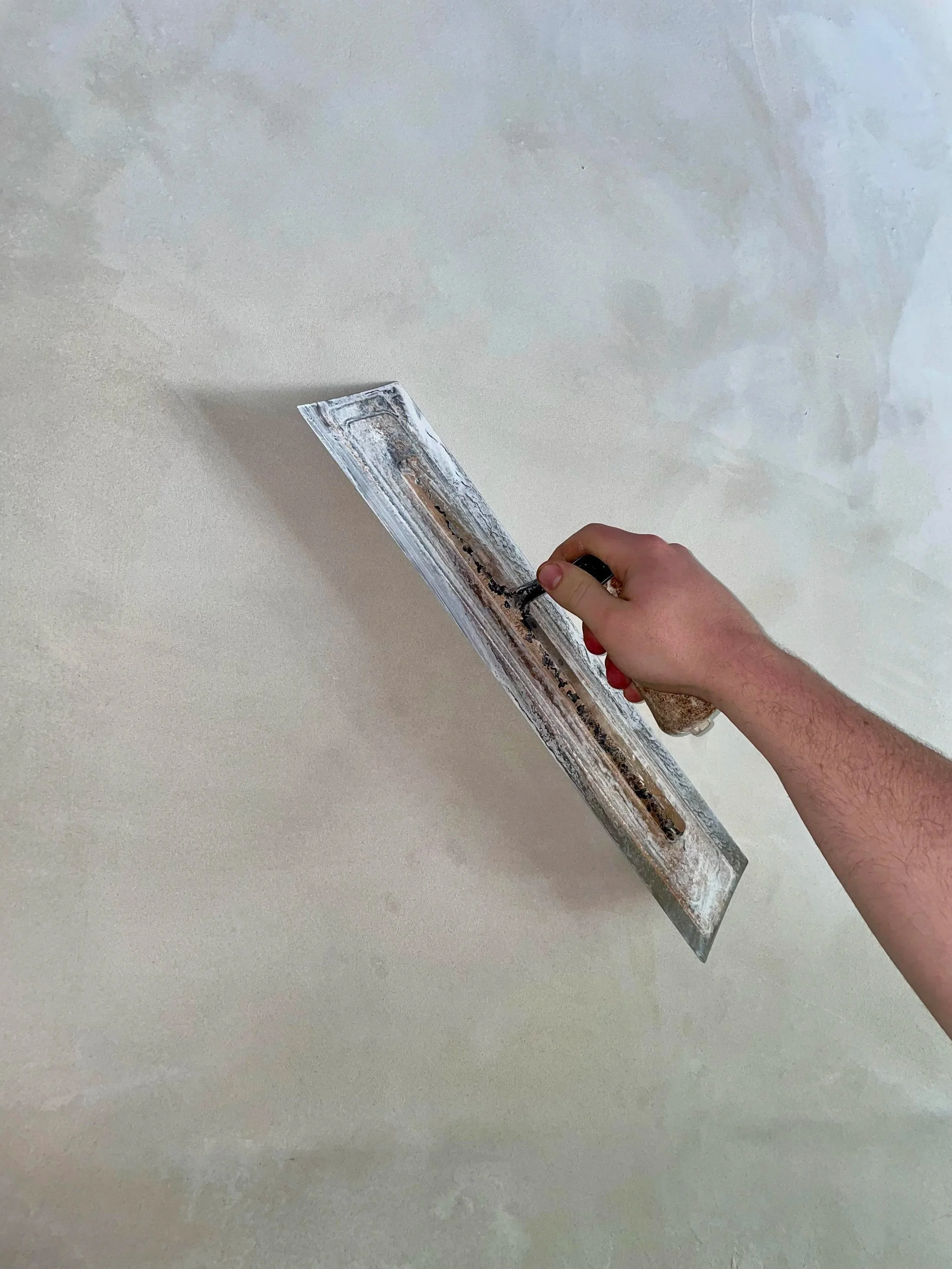 Person using a notched trowel to spread adhesive or compound on a surface.