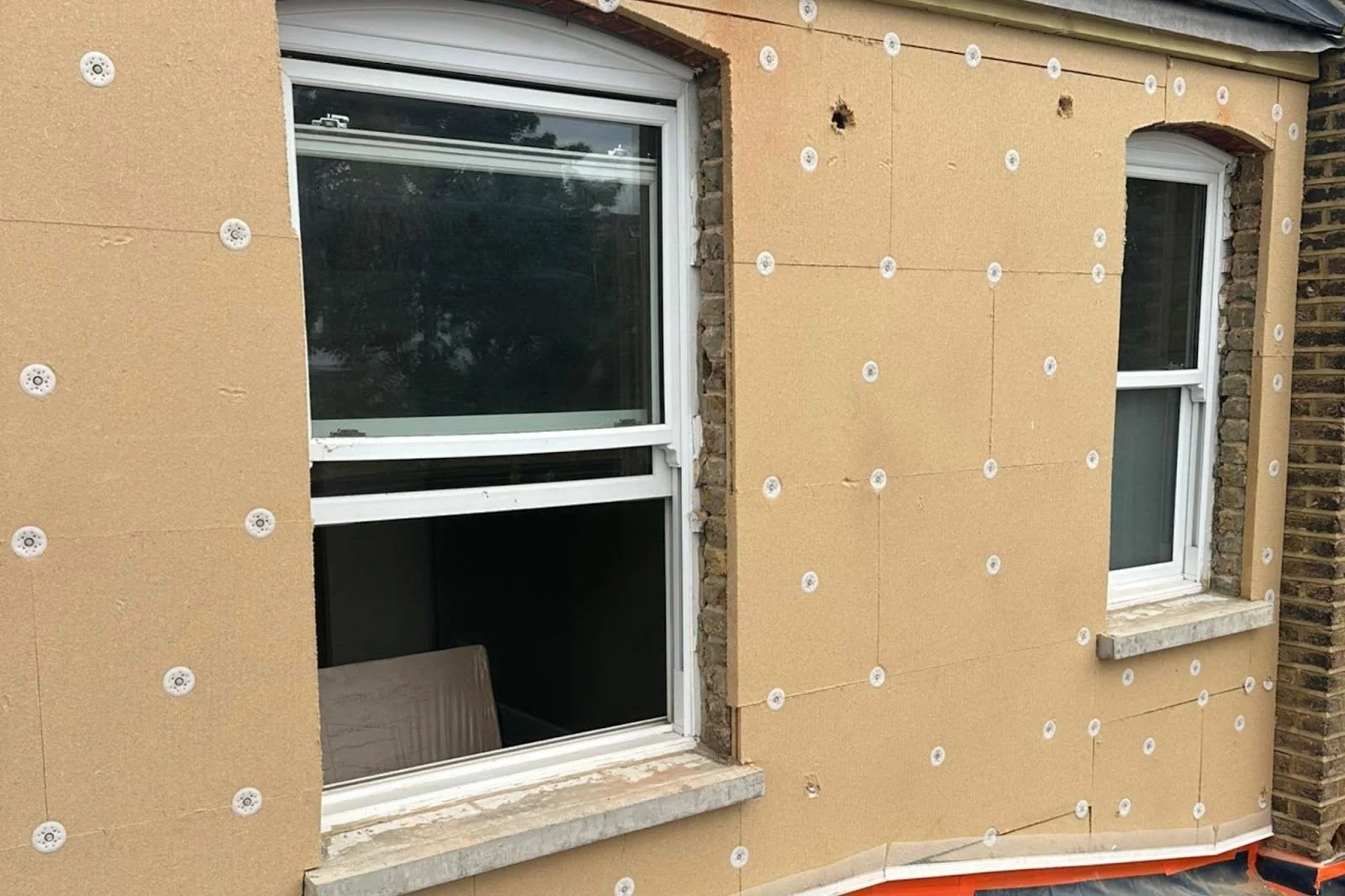 Exterior of a building under renovation with new window frames and insulation panels installed on the walls.