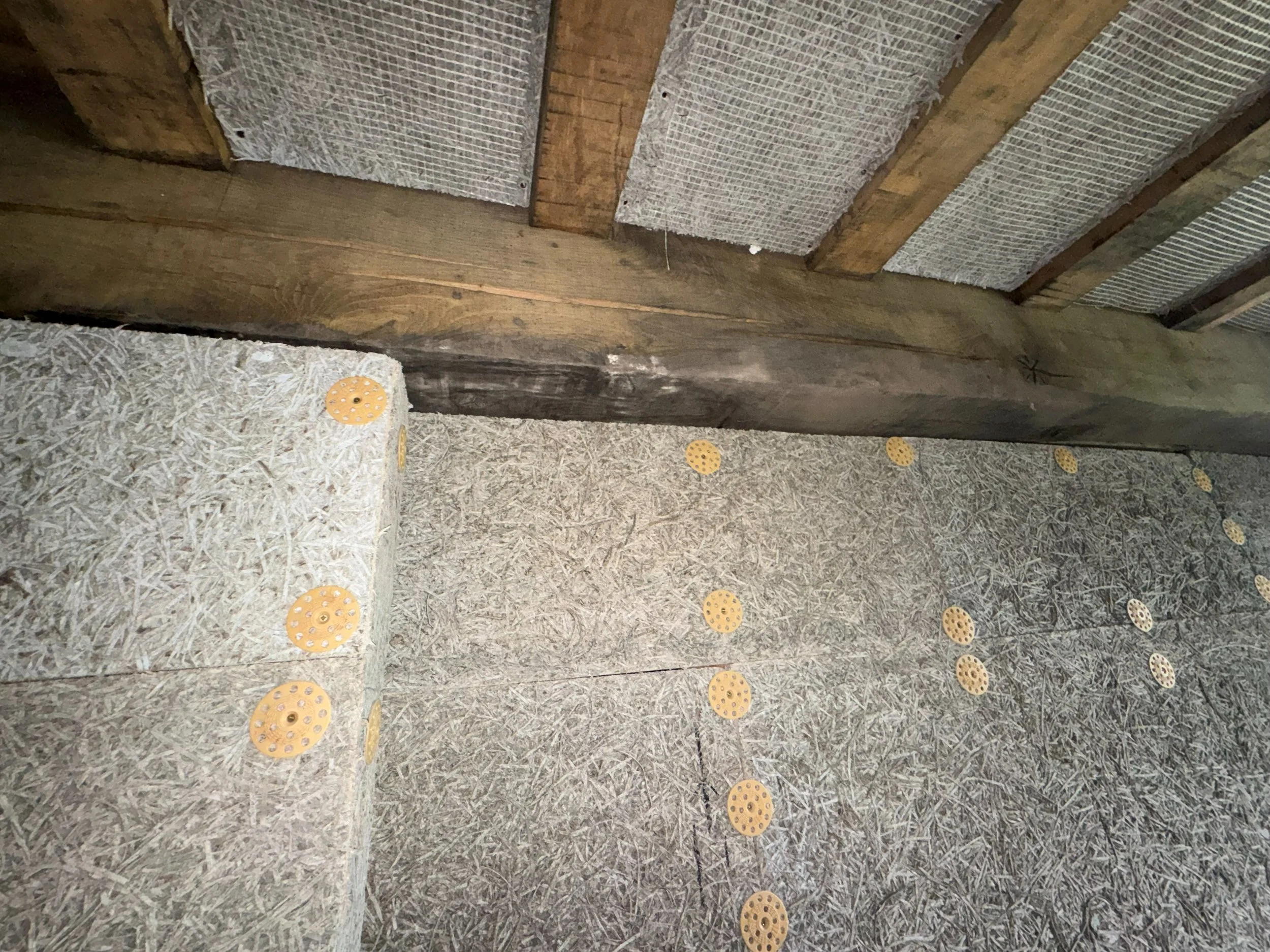 Wooden ceiling with insulation and yellow plastic spacers attached to particle board.