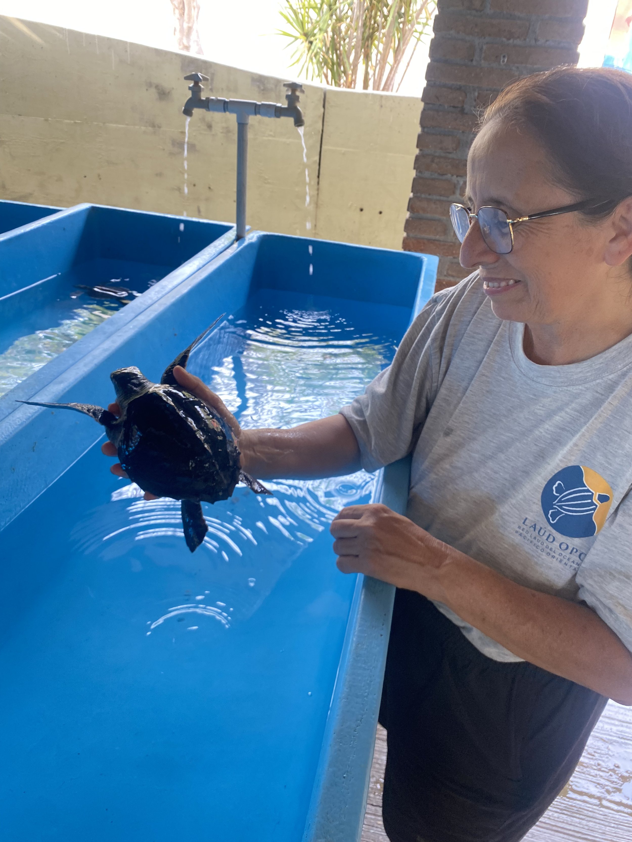 Woman holding a fish in her hand at a blue container with water and a water tap in the background.