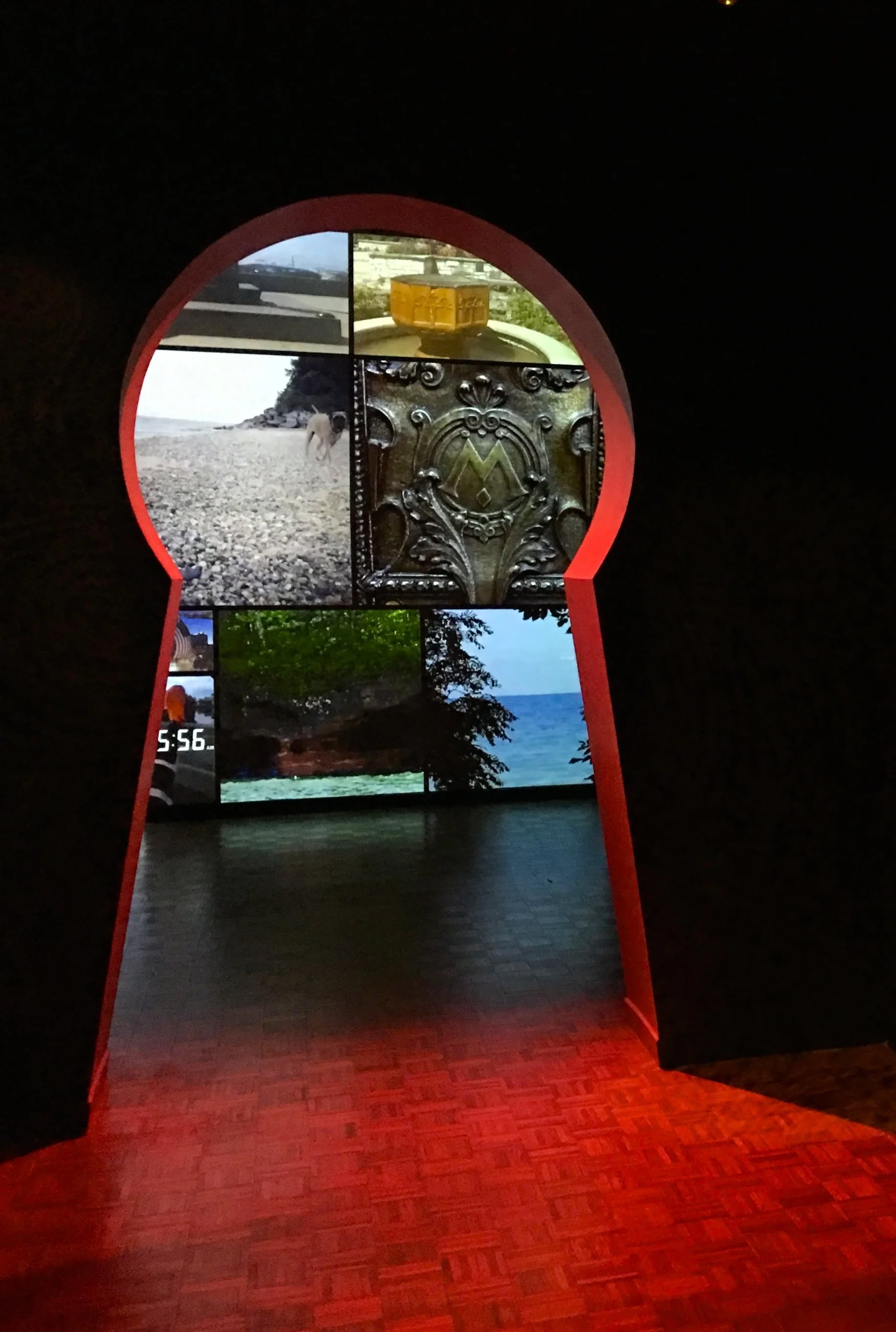 View through an arched window with multiple pictures of outdoor scenes, including a beach, trees, and a body of water, with a wooden floor in the foreground.
