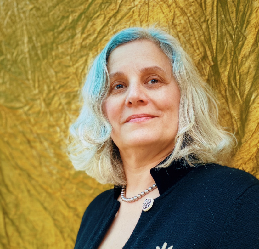 A woman with shoulder-length blonde hair, some dyed blue, standing in front of a textured yellow and green background.