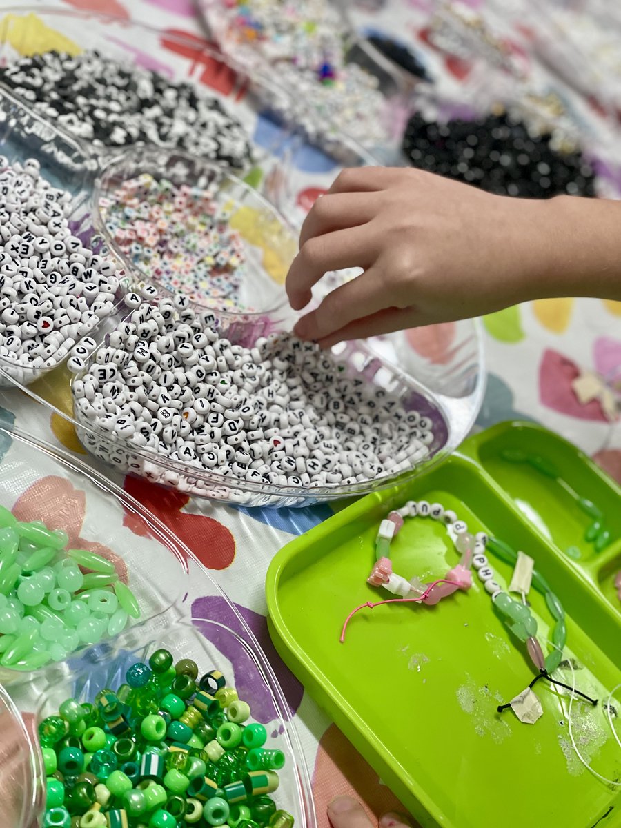 A person creating jewelry with white alphabet beads and other colorful beads on a table.