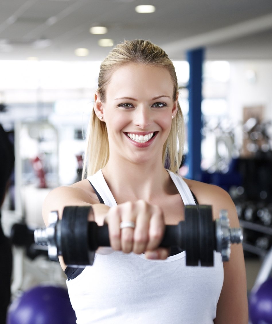A smiling woman holding a weight in a gym.