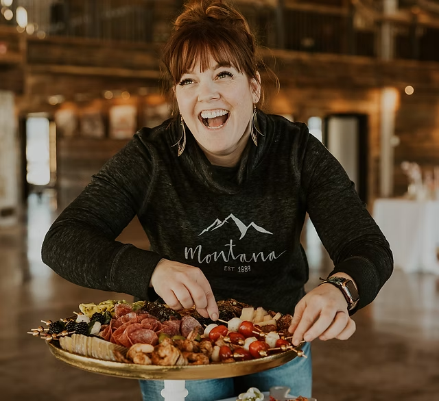 A woman with red hair smiling while reaching for food on a large platter at a restaurant or event space.