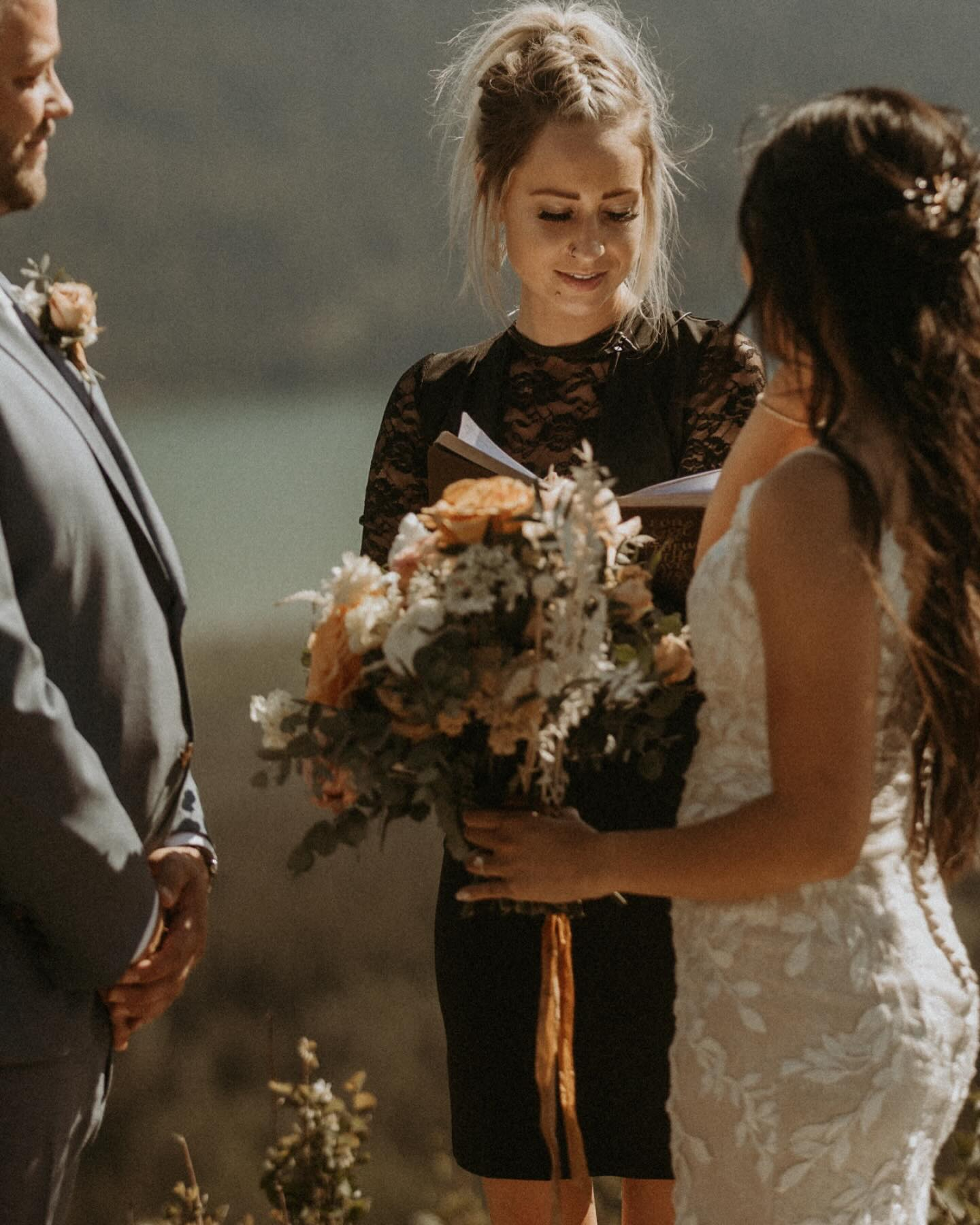 A woman in a black lace dress holding a bouquet of flowers during her wedding ceremony, exchanging vows with a bride in a white lace dress.