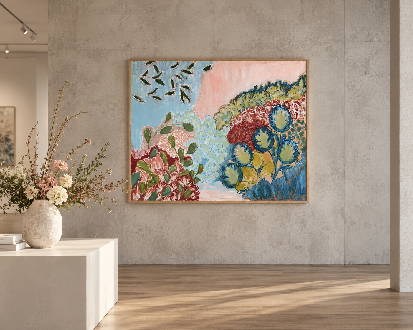An art gallery features an abstract floral painting on a grey concrete wall and a white display table with a large beige ceramic vase filled with pink and white flowers and greenery.