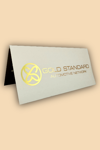 A folded greeting card with a logo and text that reads 'GOLD STANDARD AUTOMOTIVE NETWORK' in gold and bronze colors on a light background.