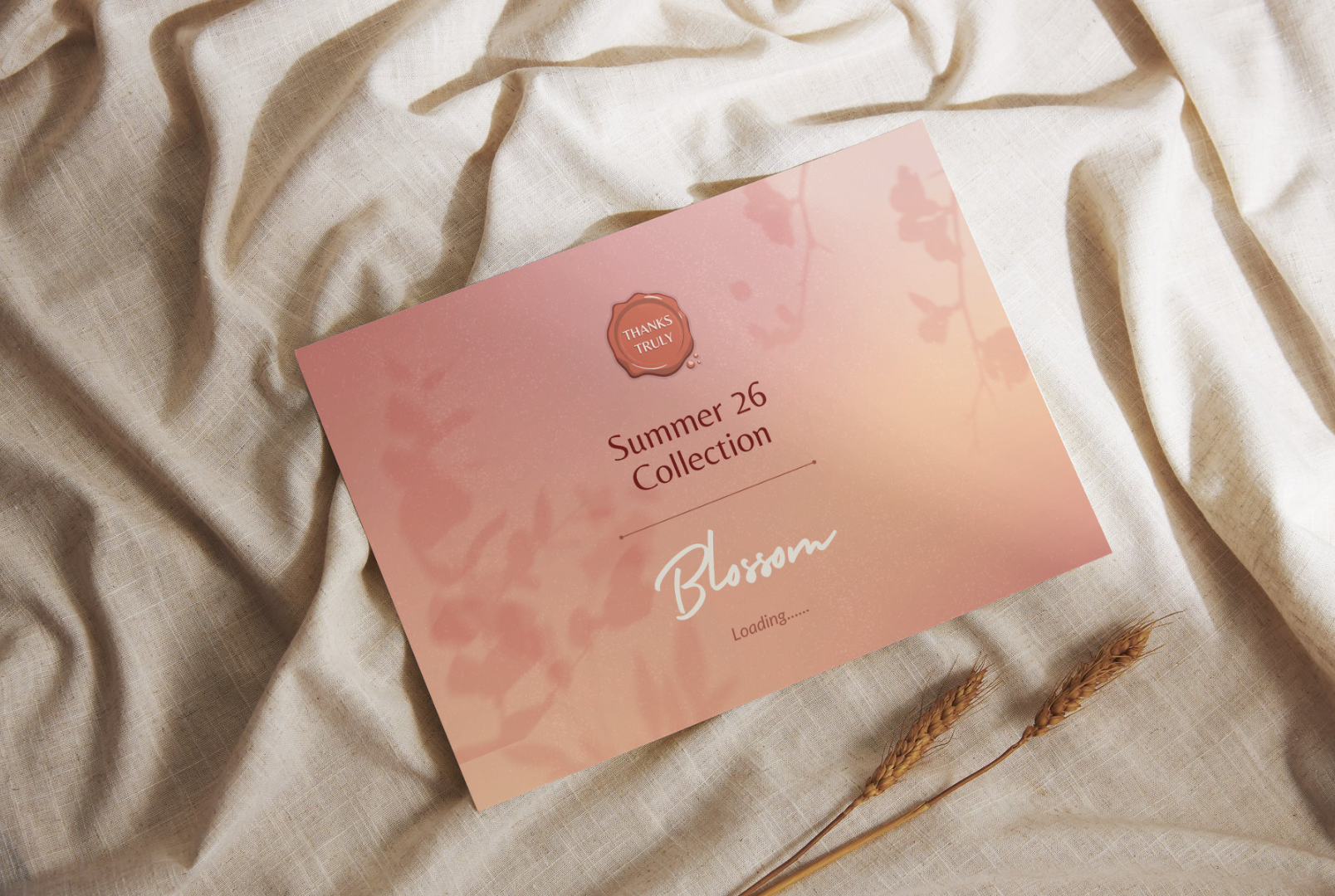 A pink and orange gradient card with the words 'Summer 26 Collection Blossom' is placed on beige fabric with some wheat stalks nearby. The card has a decorative seal that says 'Thanks Truly' and a loading indicator.