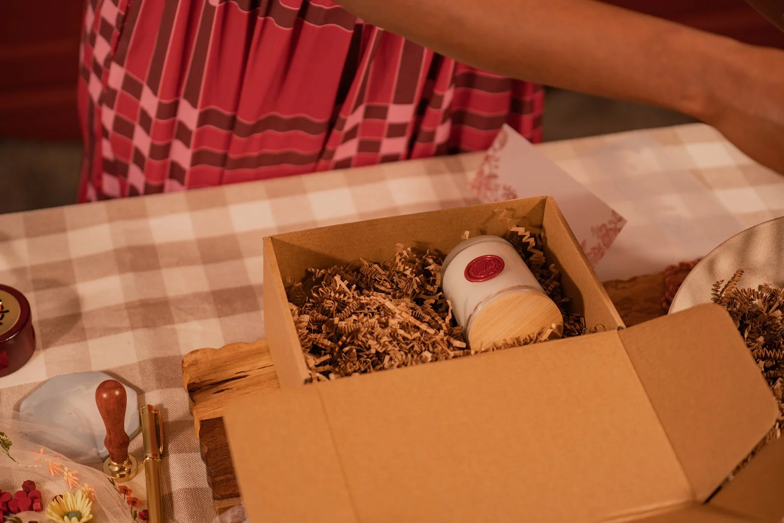 A gift box filled with crinkled paper, containing a small white jar with a red wax seal on top.
