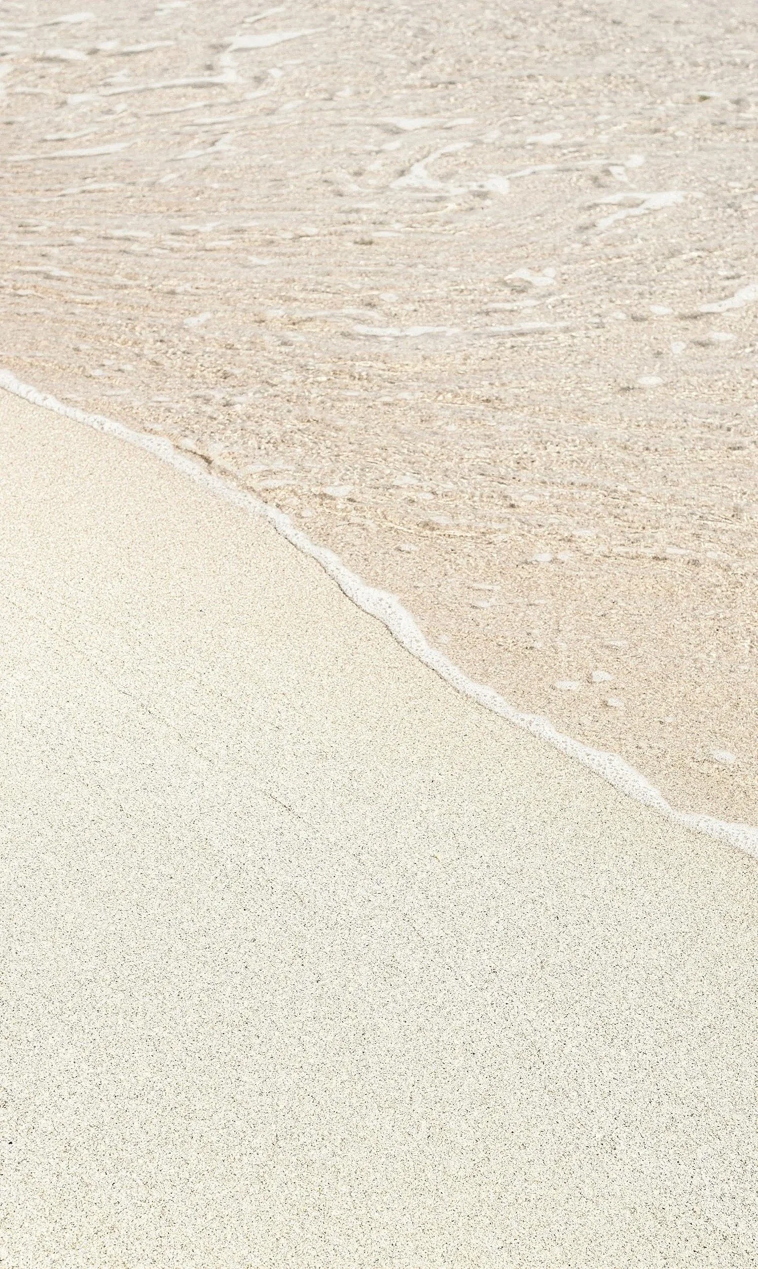 Close-up of waves washing onto a sandy beach with light-colored sand and gentle water motion.