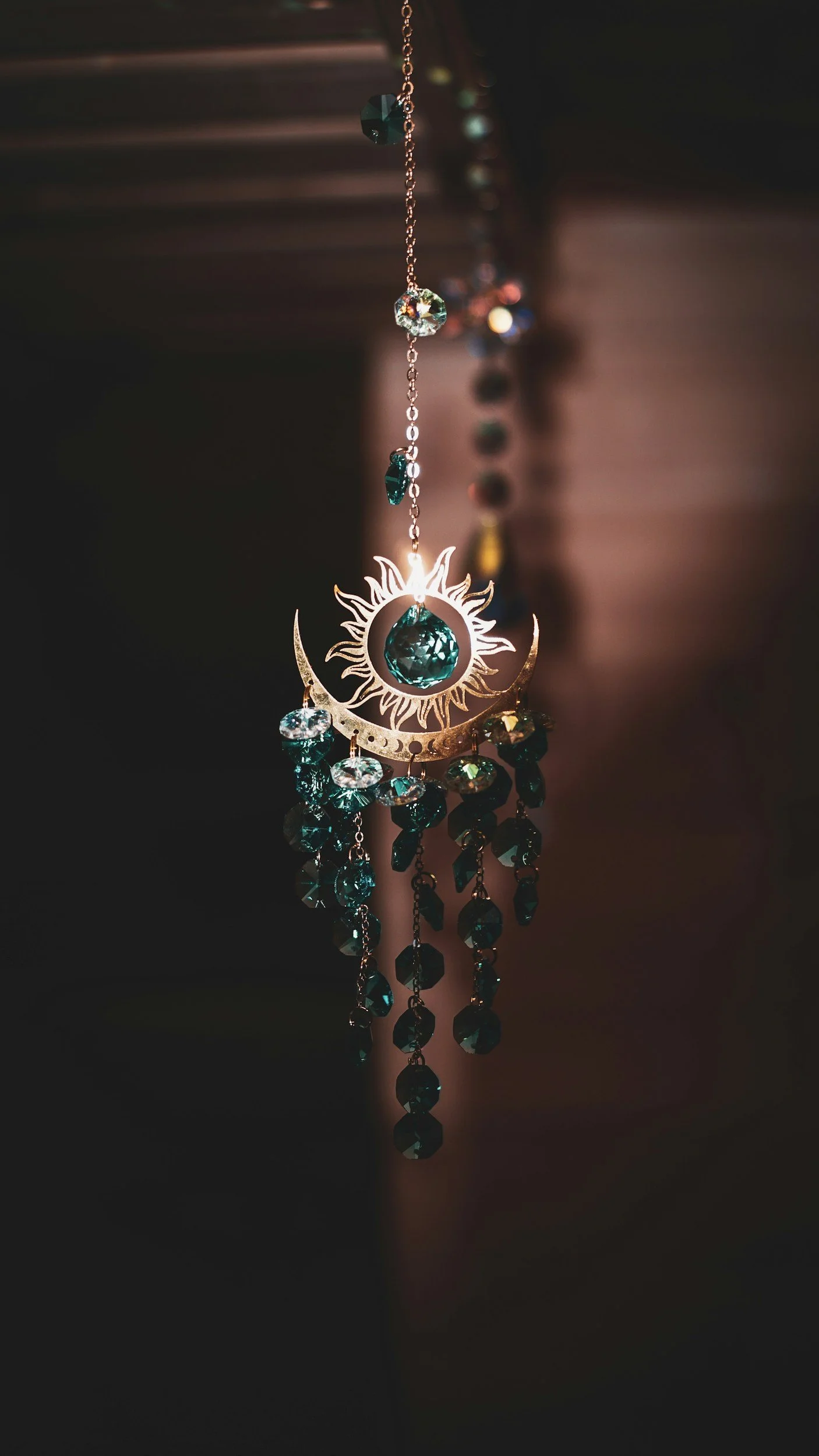 A beaded sun catcher mostly in shadow with only a little light shining on the main element.