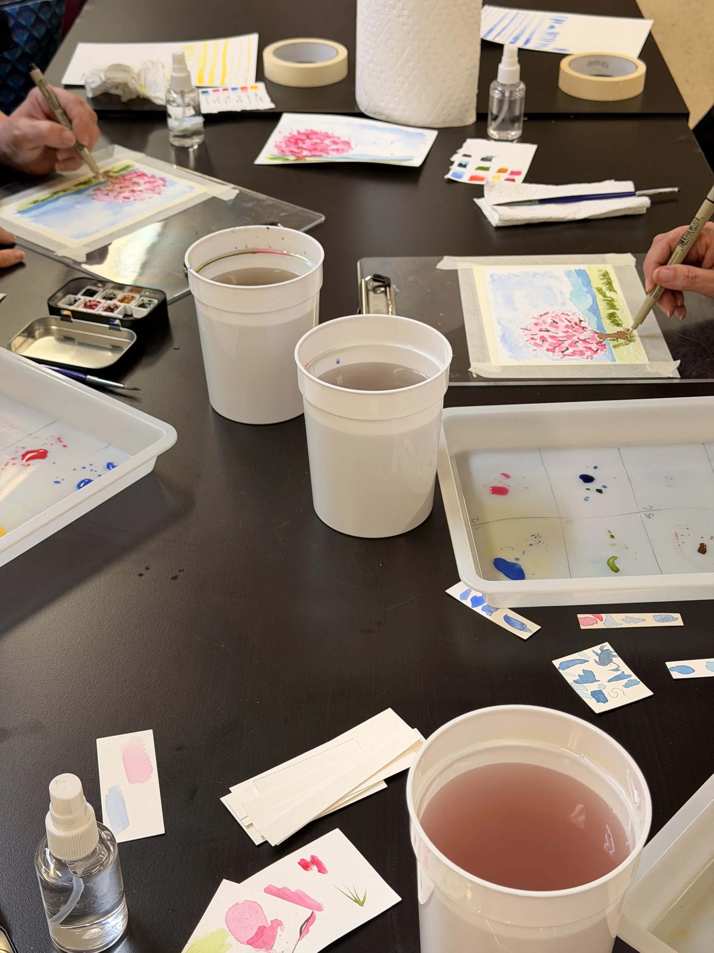 Watercolor paintings and painting supplies on a studio table.