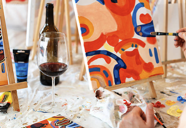 Alfonso Soler/iStock - Closeup on an acrylic painting and a glass of wine with a bottle and other easels in the background.