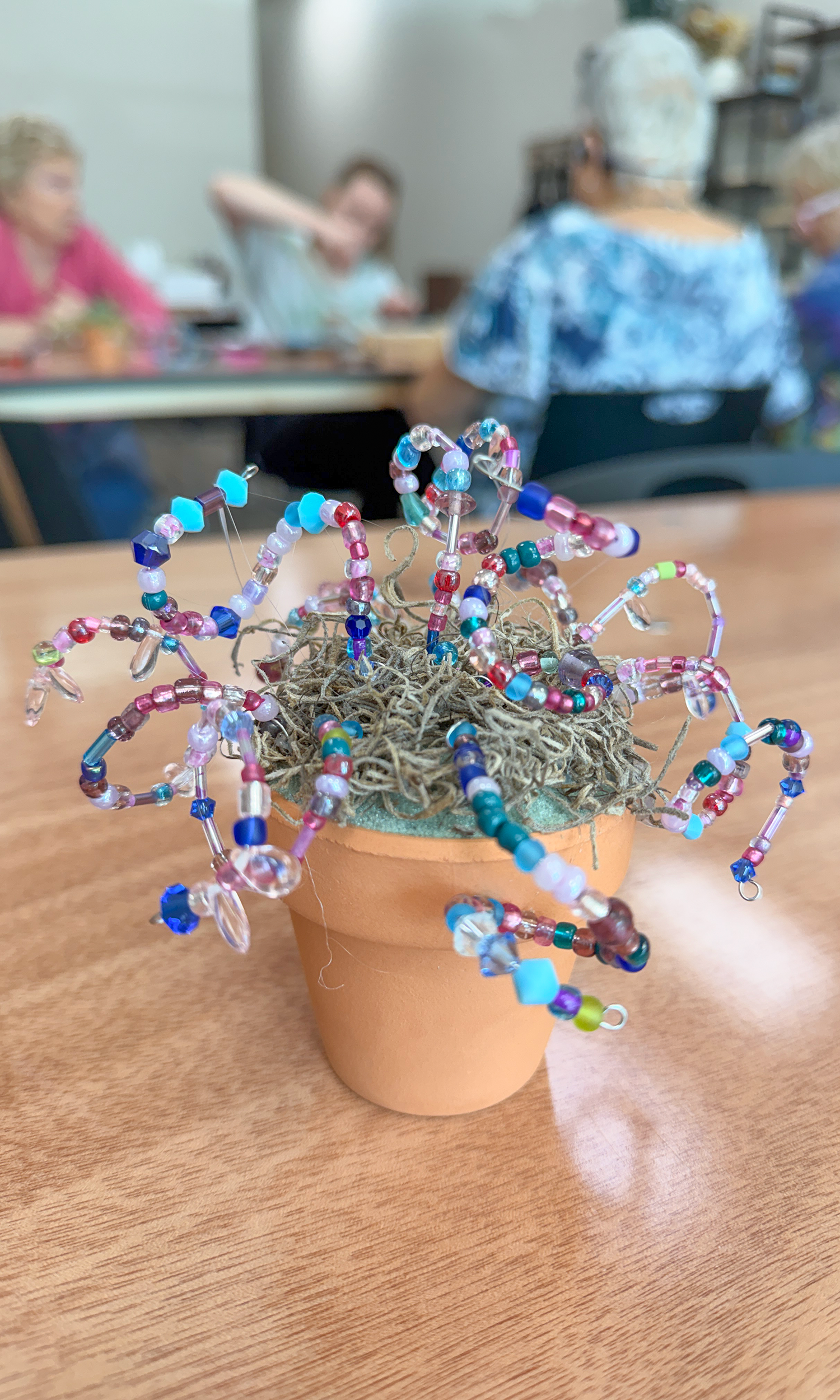 Close up on a beaded plant sitting on table with art students in the background.
