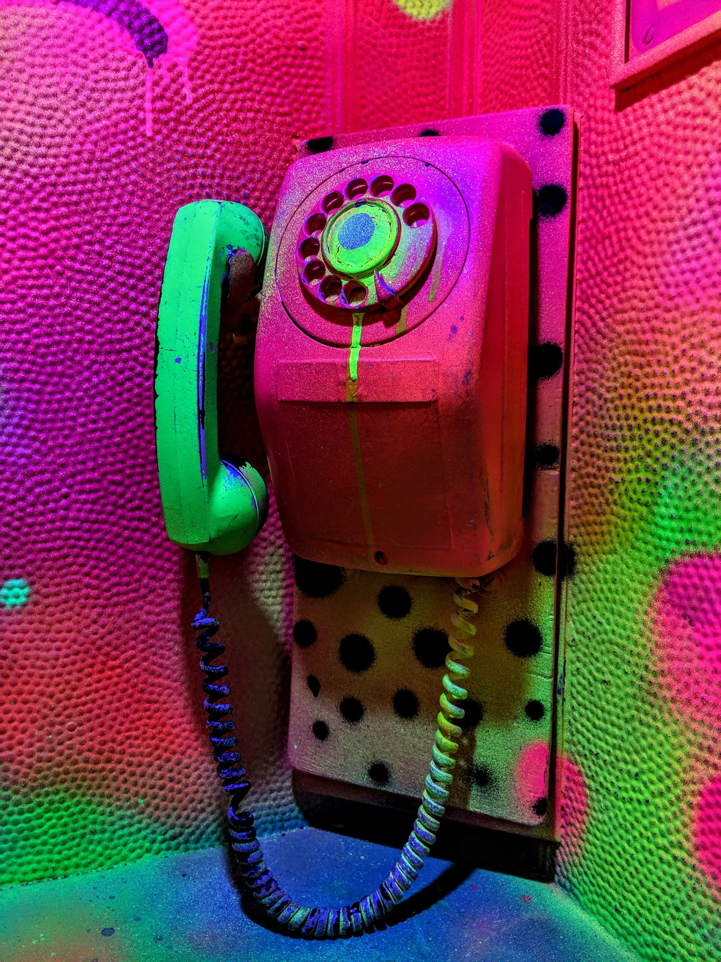 A vintage rotary dial telephone mounted on a colorful, textured wall with vibrant neon lighting.