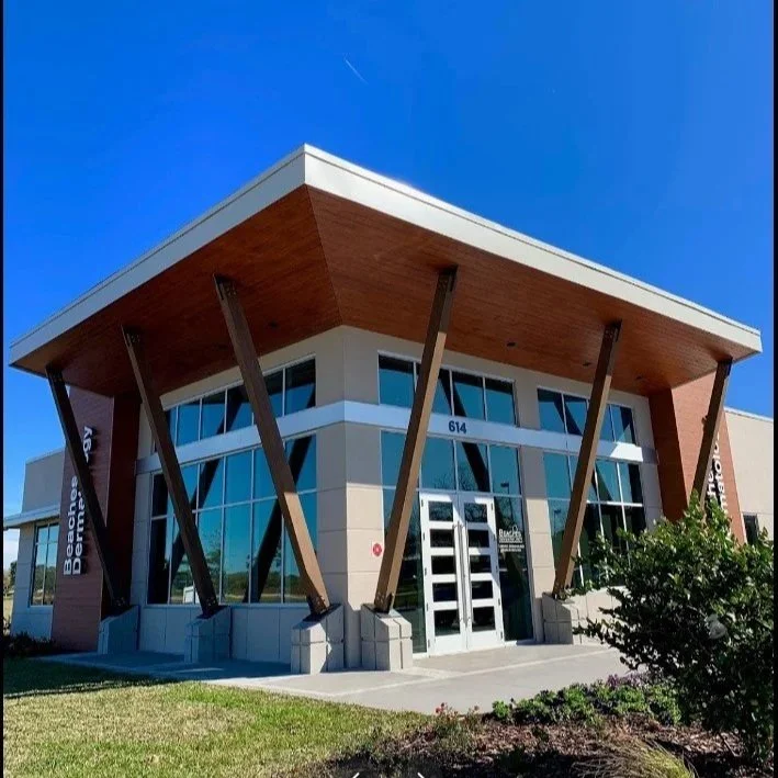 Modern commercial building with large glass windows, angled support beams, and wooden accents on the roof, located at 614 with blue skies above.