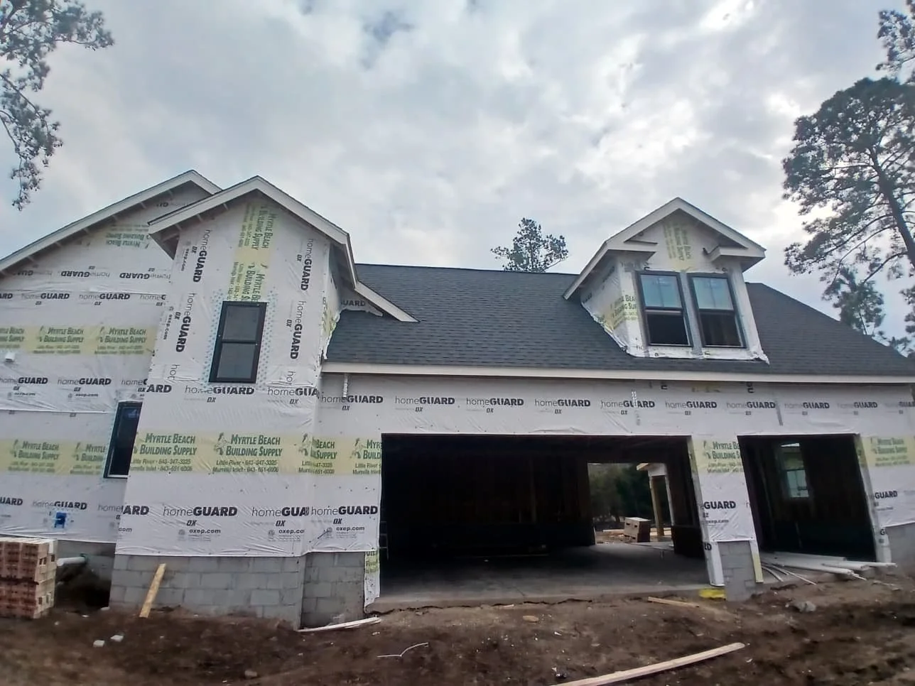 Under construction house with scaffolding, exposed windows, and construction materials around the site, during cloudy weather.