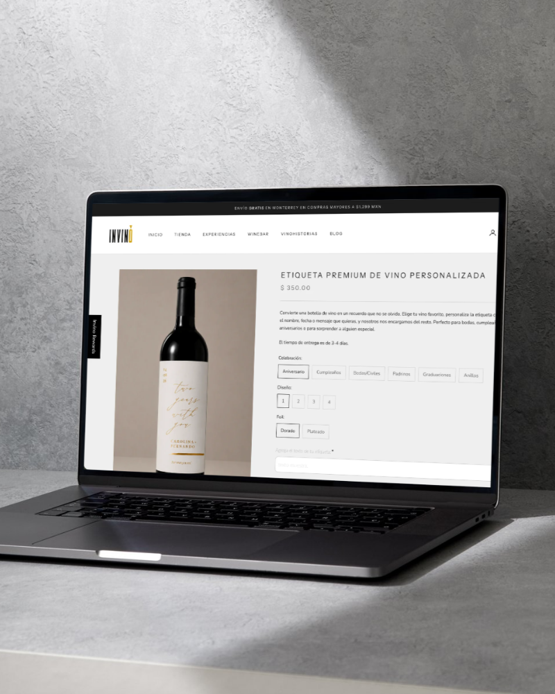 A laptop on a gray desk displaying a website for ordering personalized wine labels, with a picture of a wine bottle and options for customization.