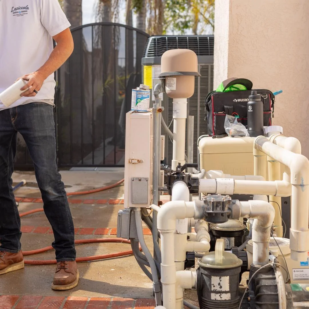 Pool equipment setup with pipes, pumps, and filtration system on a patio, with a person holding a container on the left.