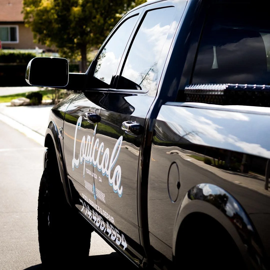 Black service vehicle with white and blue lettering, parked on a suburban street under cloudy skies.