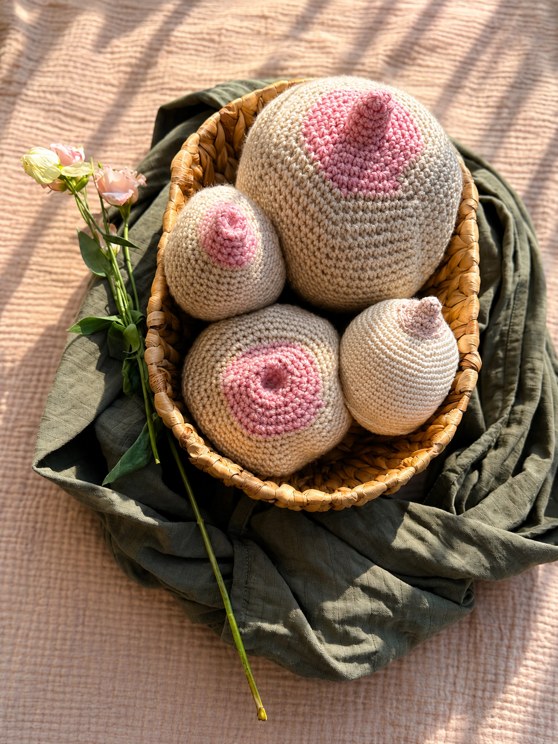 Handgestrickte, rosa und weiße unscharfe Pilzdekorationen in einer Korb auf einem Tuch, mit Blumen daneben.