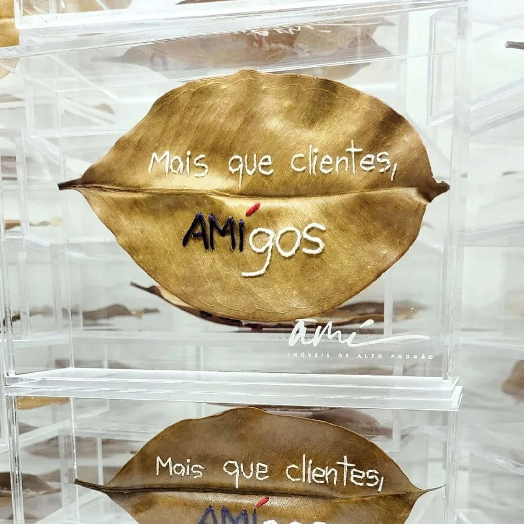 Folha seca dourada com mensagem escrita em linhas brancas, vermelhas e pretas que diz: "Mais que clientes, amigos".