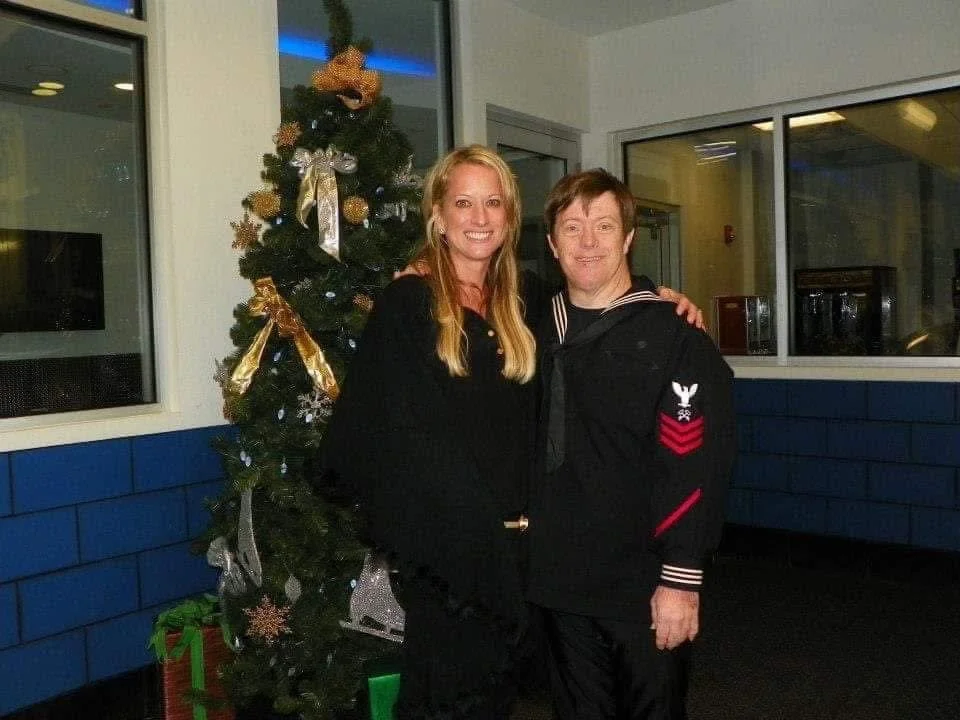 A woman and a man standing together next to a decorated Christmas tree, smiling at the camera.
