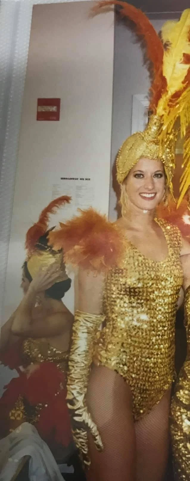 Woman in a gold and yellow costume with feathers, wearing a headpiece, and a glove during a performance or parade.