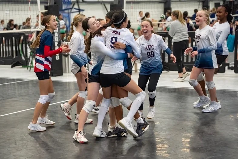 Girls volleyball team celebrating on indoor court.