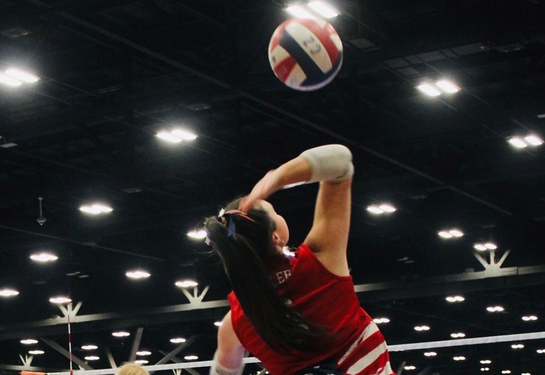 A female volleyball player in a red uniform preparing to hit the volleyball in an indoor sports facility.