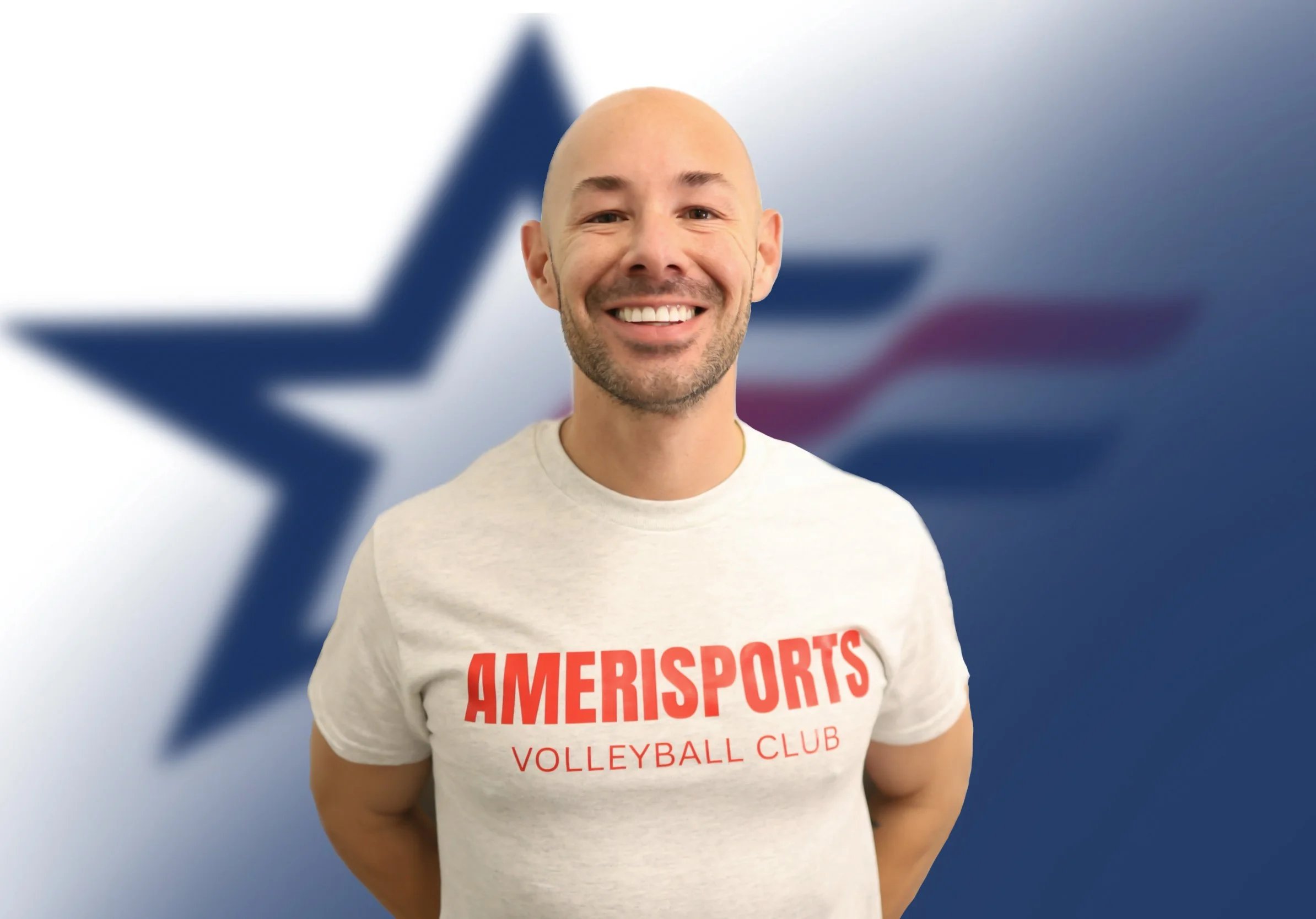 Smiling man with a shaved head and beard wearing a light-colored T-shirt with red text reading 'AMERISPORTS VOLLEYBALL CLUB' in front of a blurred background of the Texas flag with a blue star.