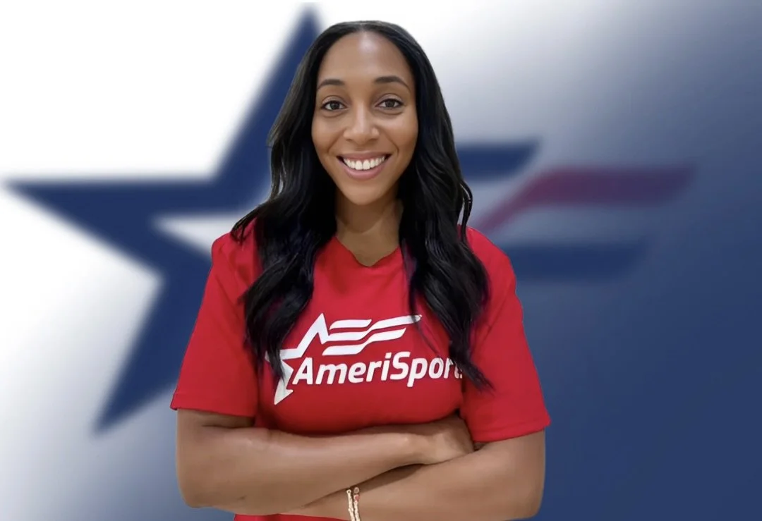 A woman in a red AmeriSport t-shirt standing with arms crossed in front of a blurred American flag background.
