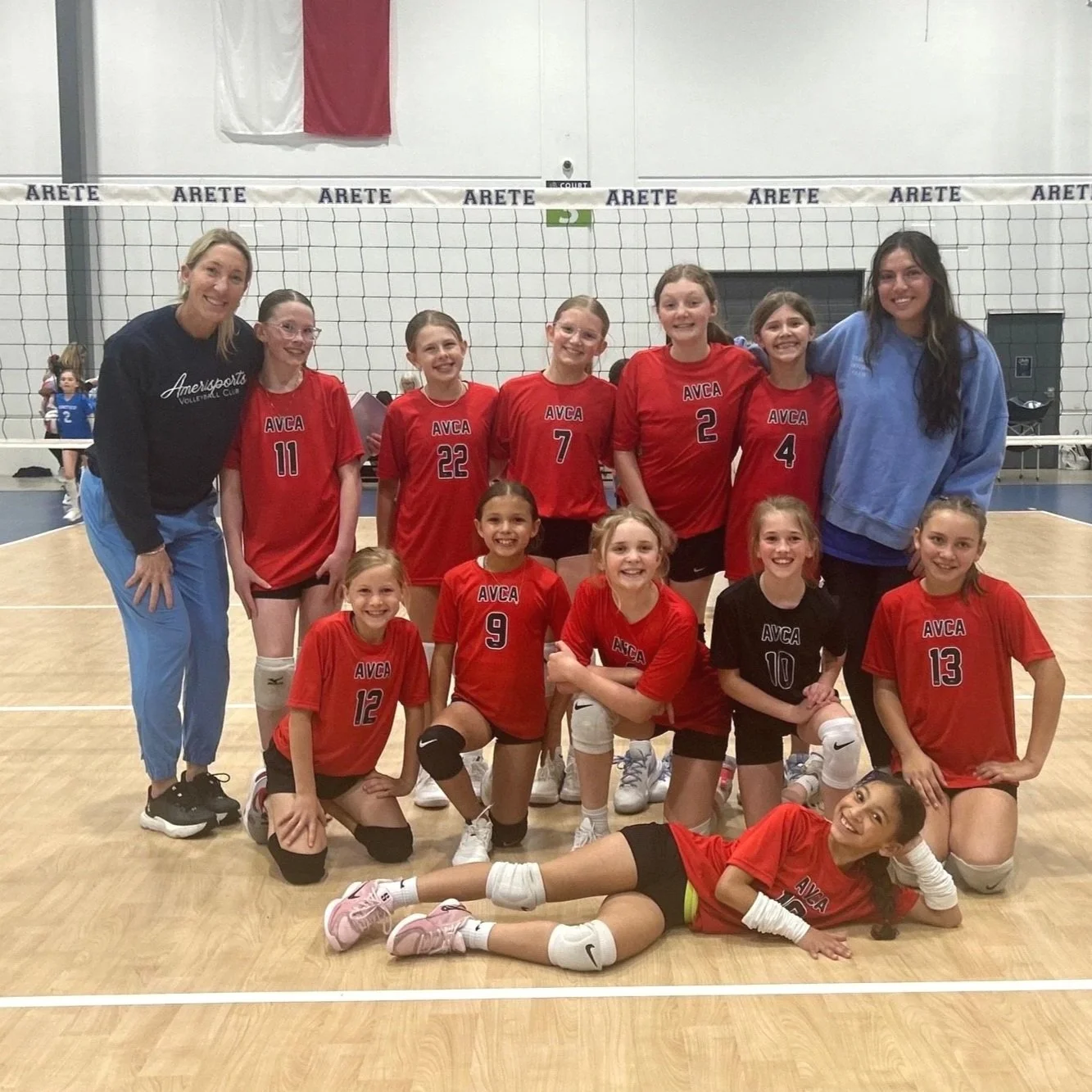 Young girls in volleyball uniforms with medals, posing with two adult women in a hallway, celebrating their achievement.