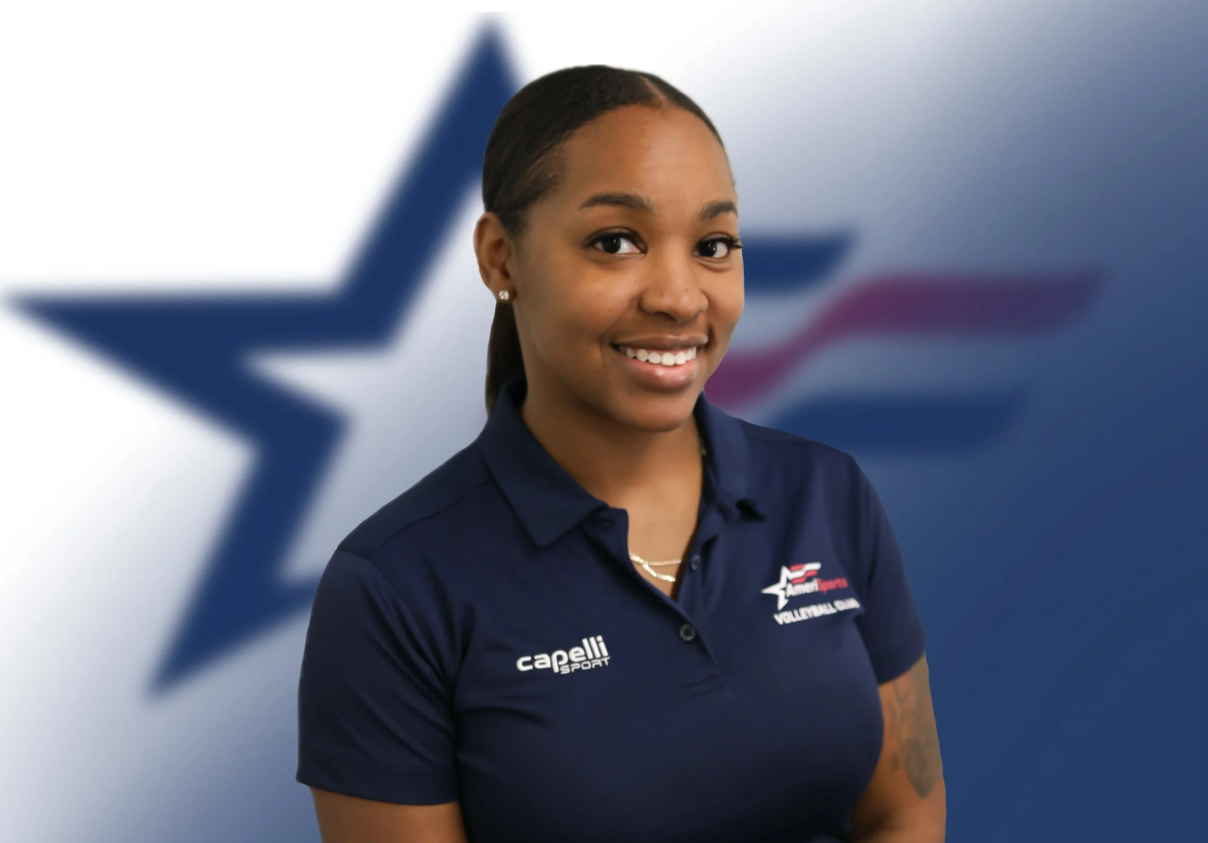 A smiling woman wearing a navy blue polo shirt with logos, standing in front of a background with a large star and American flag design.