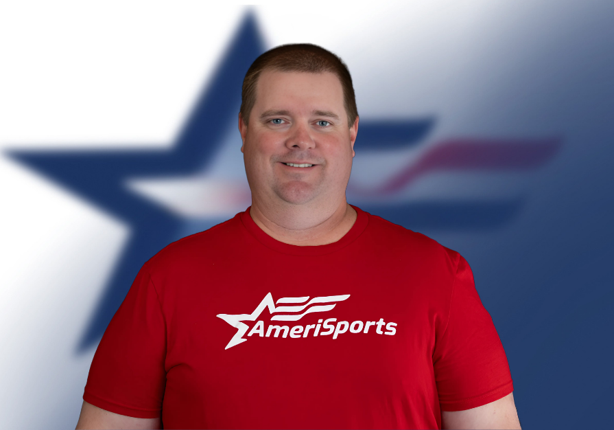 A smiling man wearing a red AmeriSports t-shirt standing in front of a blurred background with a large star and American flag design.
