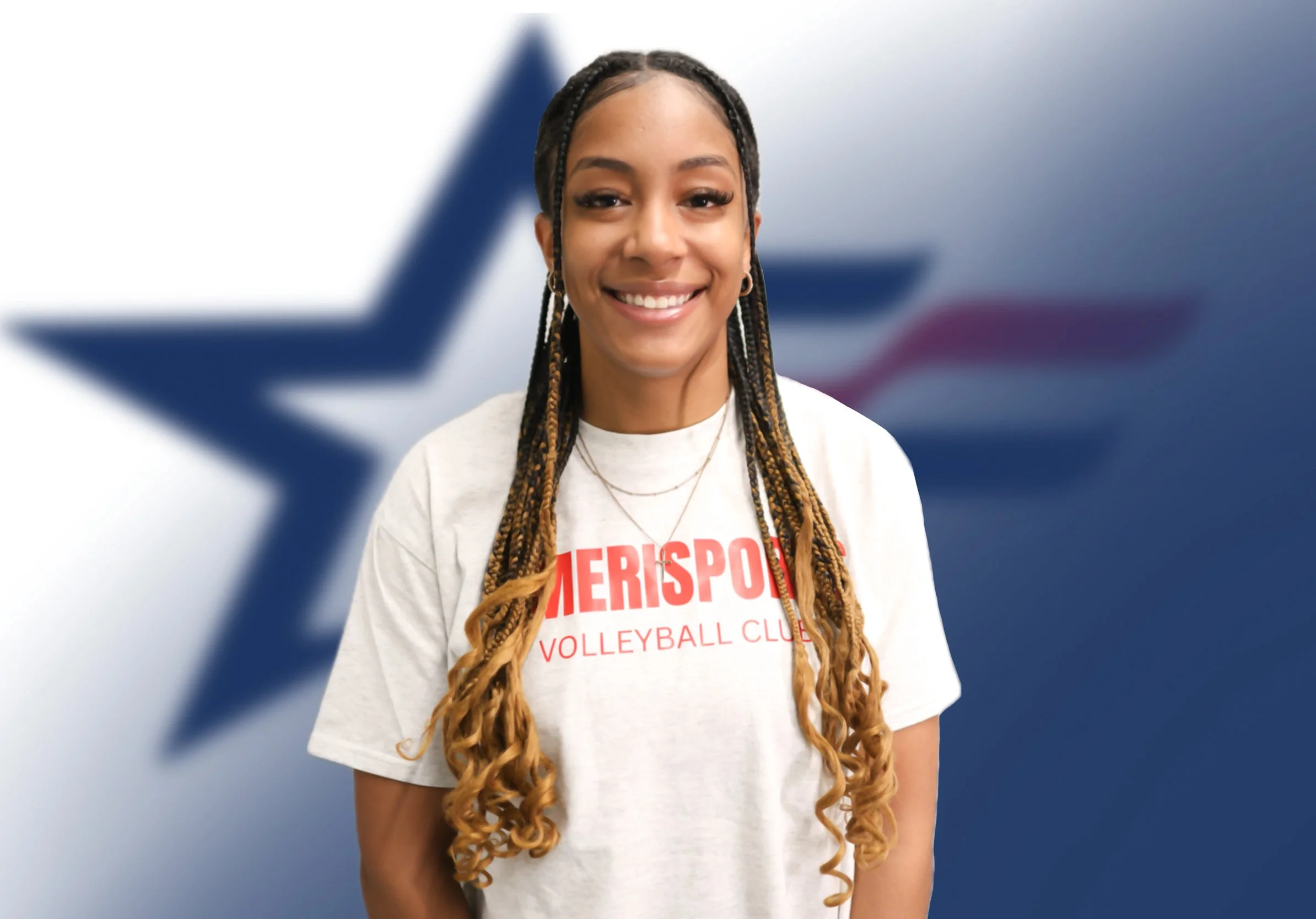 Smiling young woman with braids in front of a blurred flag with a blue star and red and white stripes.
