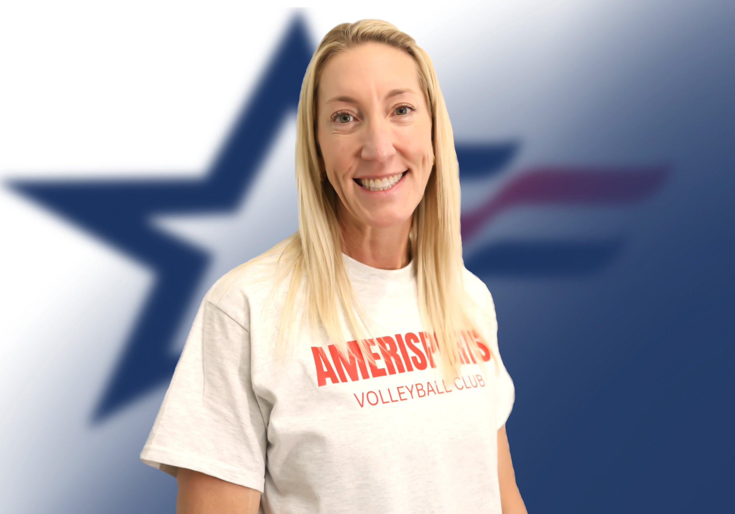 A woman with long blonde hair smiling, wearing a gray t-shirt that says 'AMERICAN SP' in red letters, standing in front of a large American flag background with a blue star.