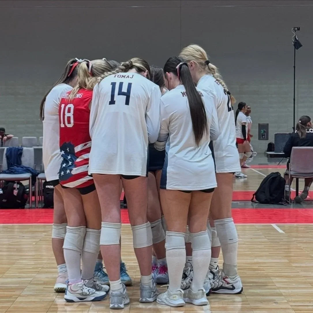 A group of female volleyball players huddled together on a court during a game or practice.