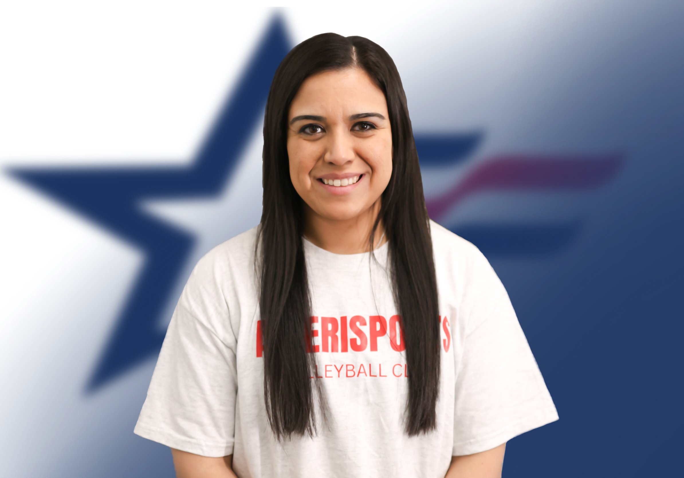 A young woman with long dark hair smiling, wearing a white t-shirt with red text, standing in front of a blurred background with a large blue star and red stripes.