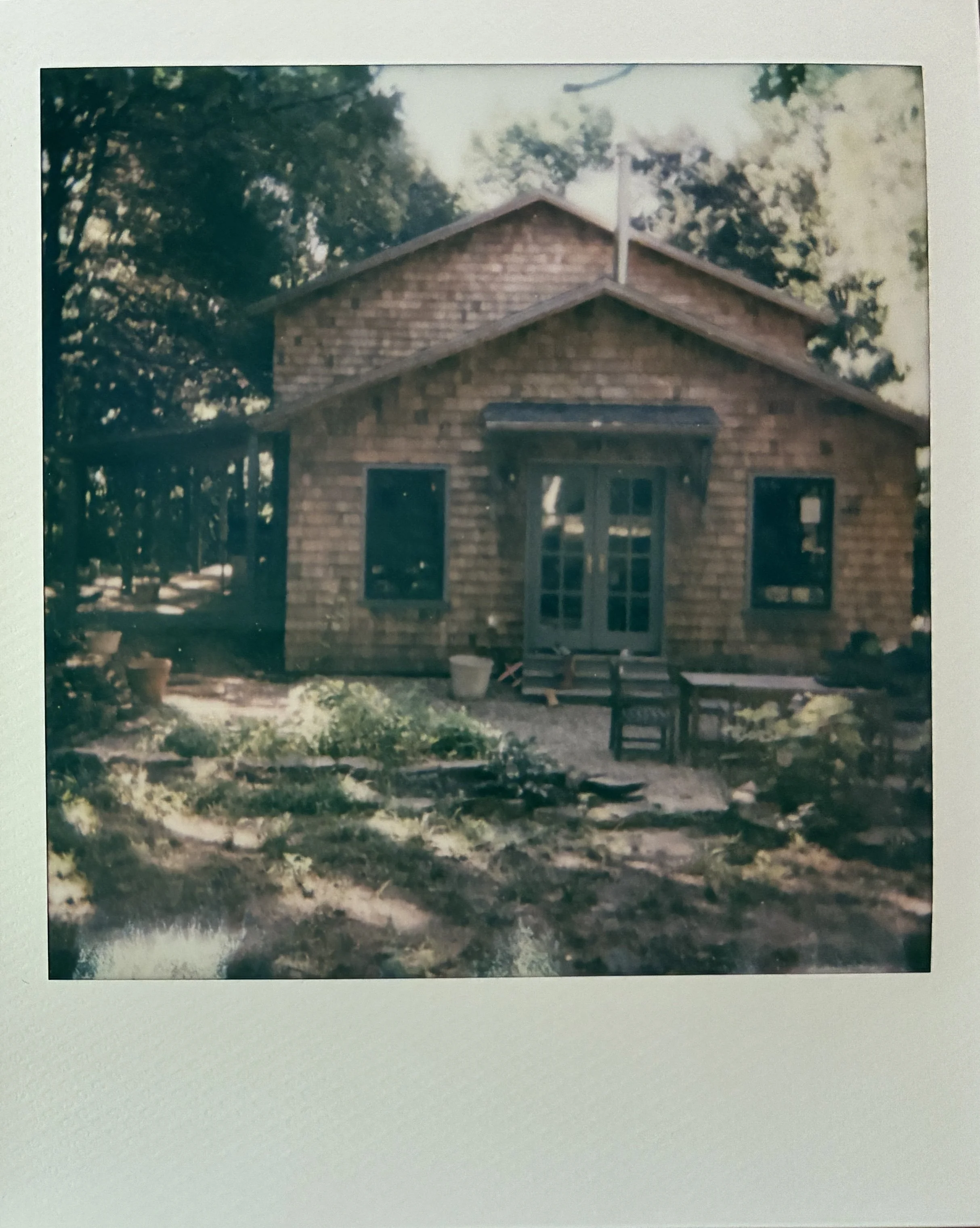 A photograph of a custom, handmade cedar shingle home in dappled sunlight, highlighting the symmetrical facade.