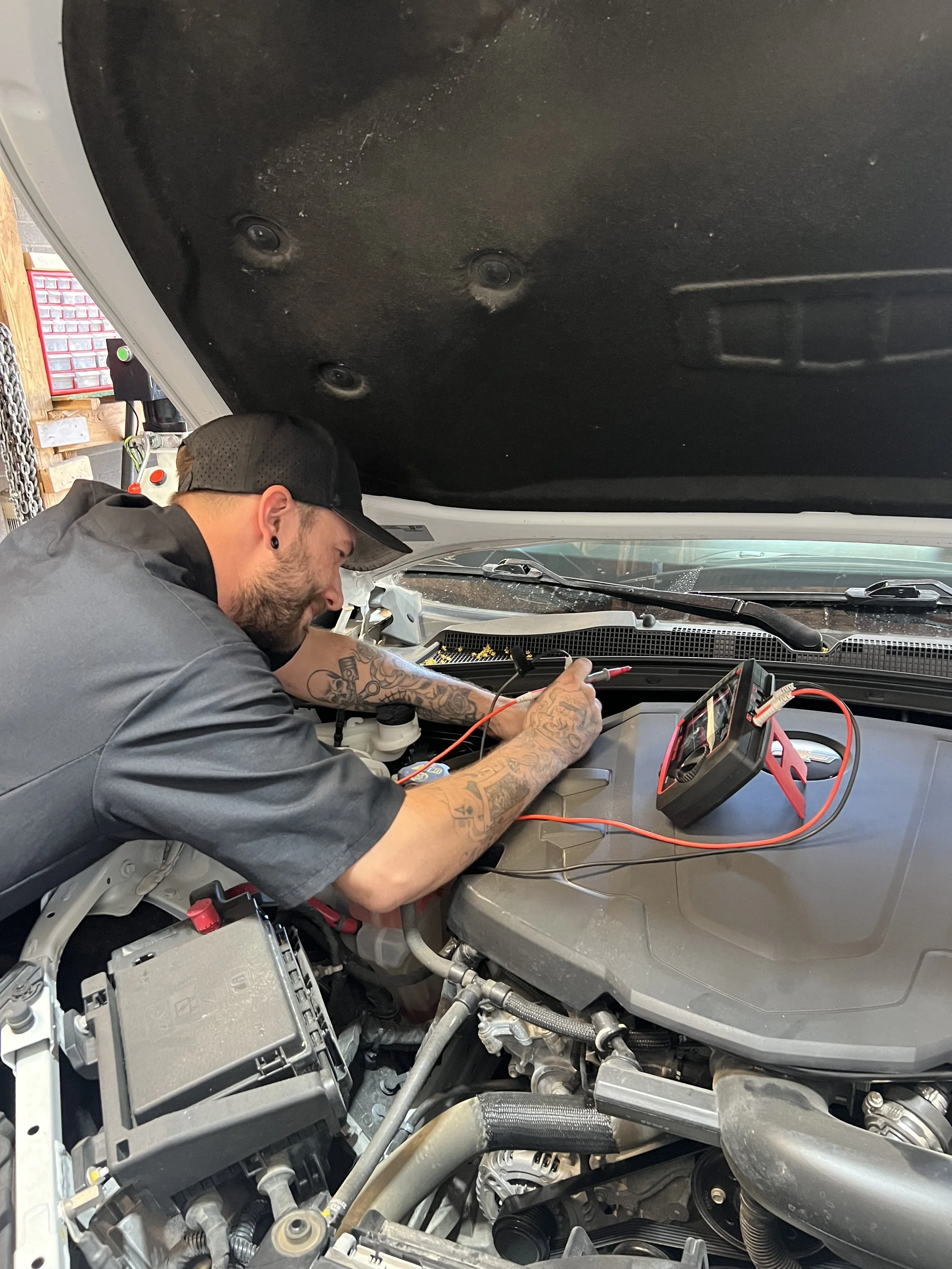 A man with tattoos working on the engine of a car in a garage.