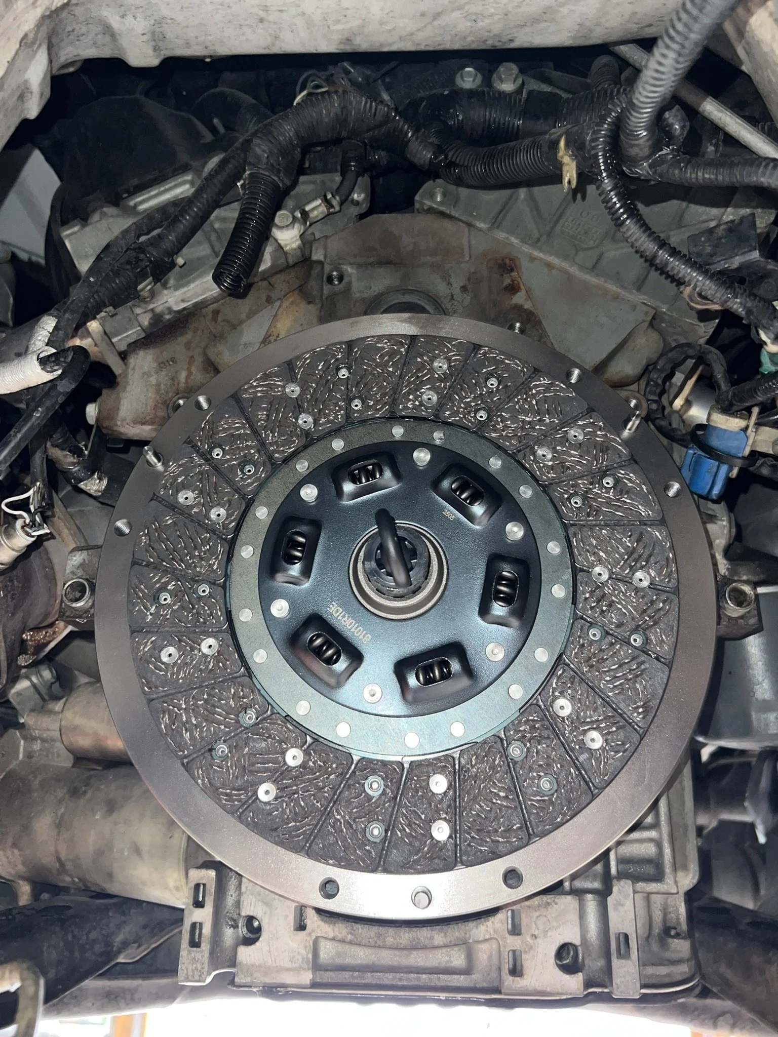 Close-up of an automotive clutch assembly showing the clutch disc and pressure plate mounted on the flywheel inside a car engine.