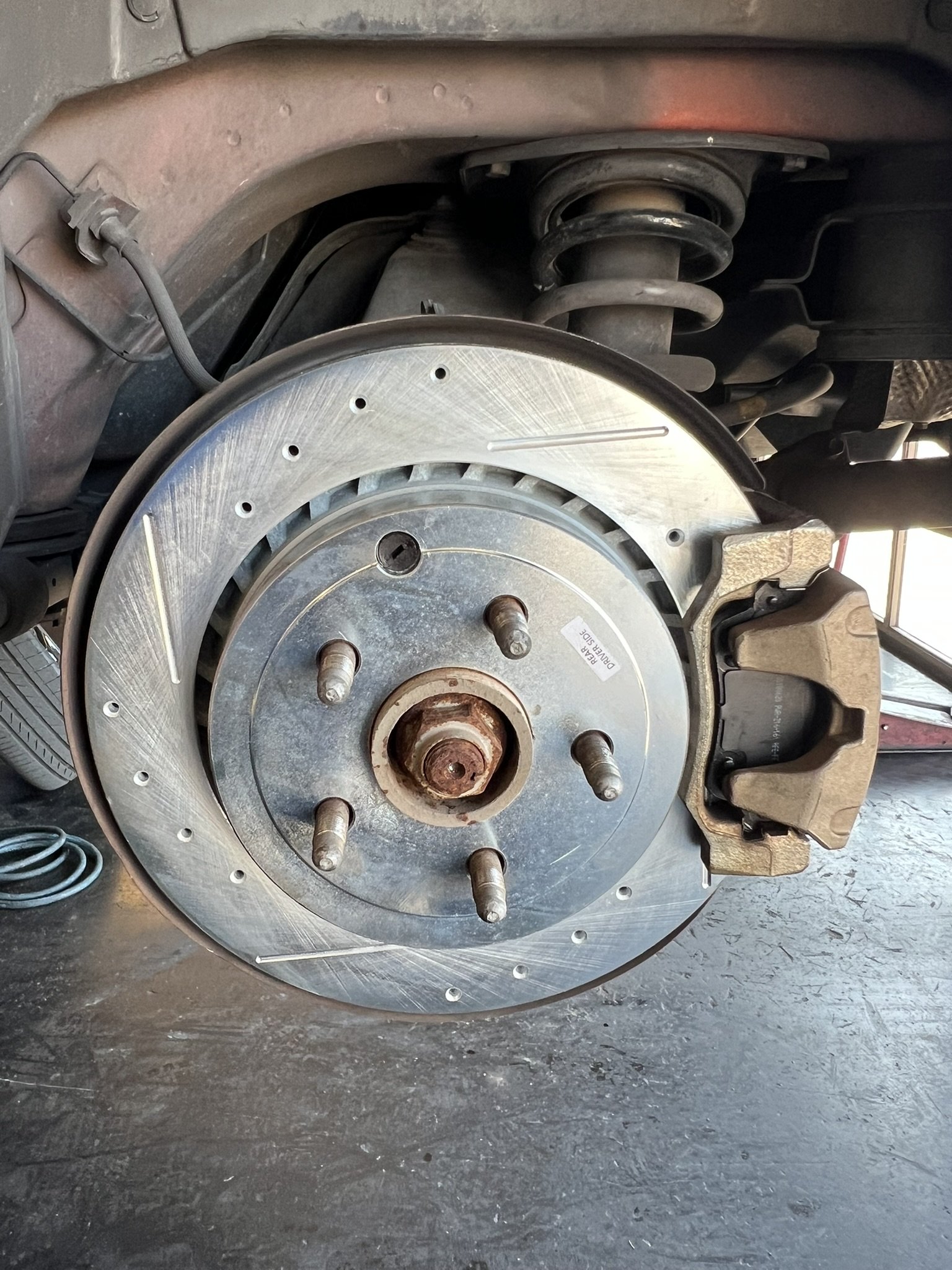 Close-up of a disassembled car wheel hub, brake disc, rotor, and brake caliper on a black workshop floor.