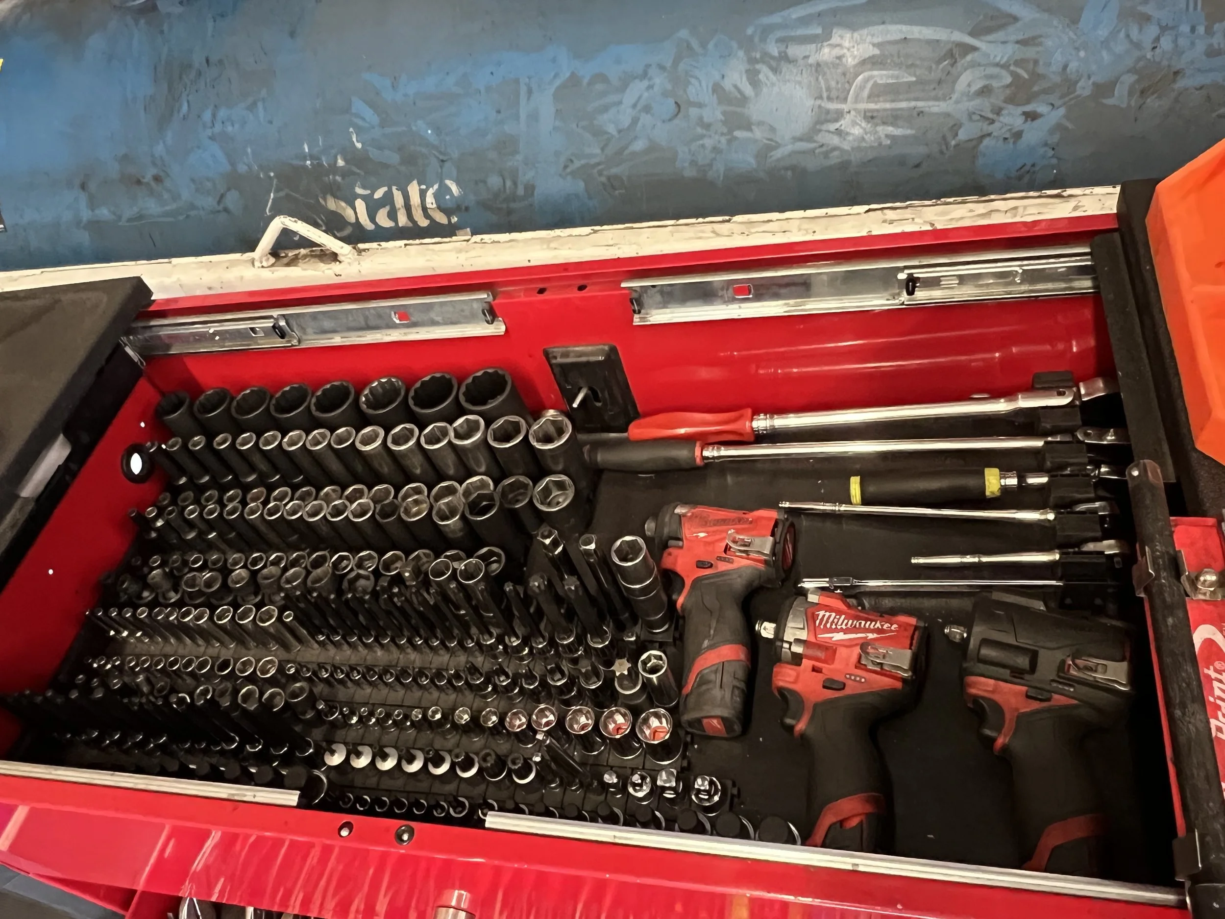 A red toolbox containing various tools, including a power drill, screwdrivers, socket wrench sockets, and extension bars.