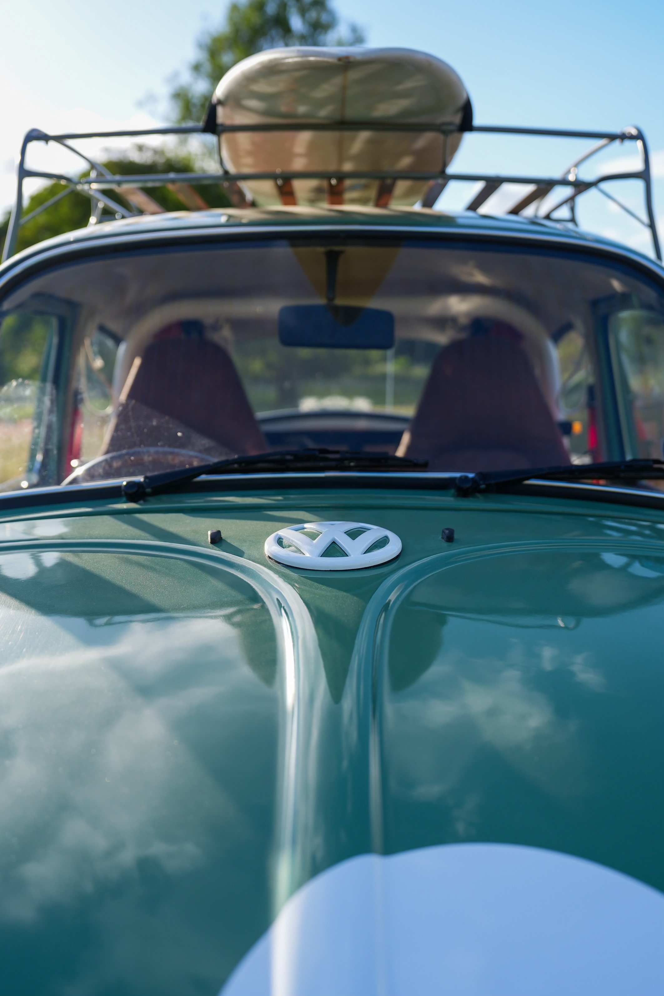 Front view of a vintage Volkswagen van with kayak on roof rack, parked outdoors on sunny day.