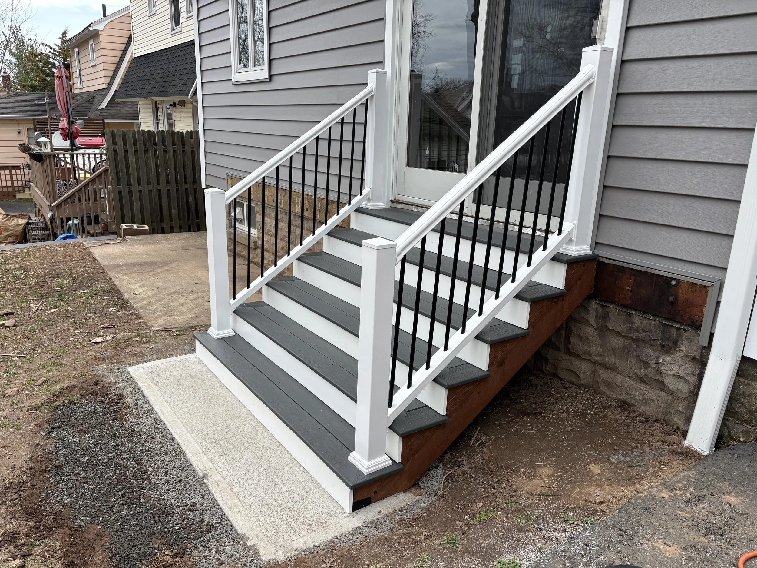 Back porch stairs with black railings and gray steps, leading to a door with a glass panel. The house has gray siding licensed Insured Bonded home improvement contractor in New Jersey